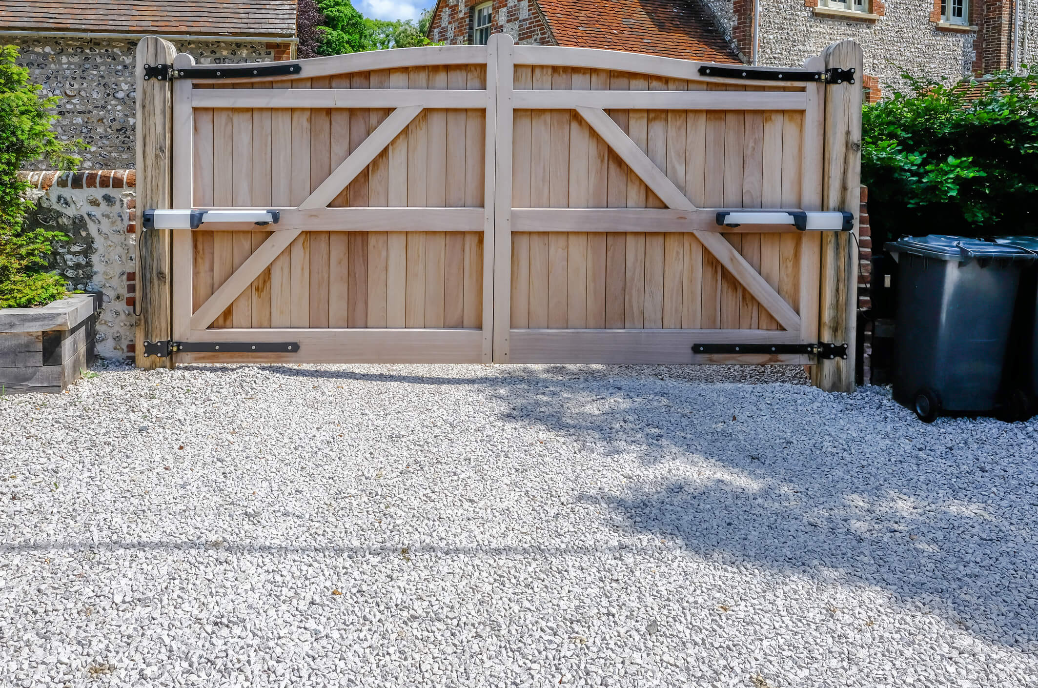 Large wooden entry electric gates with stone driveway